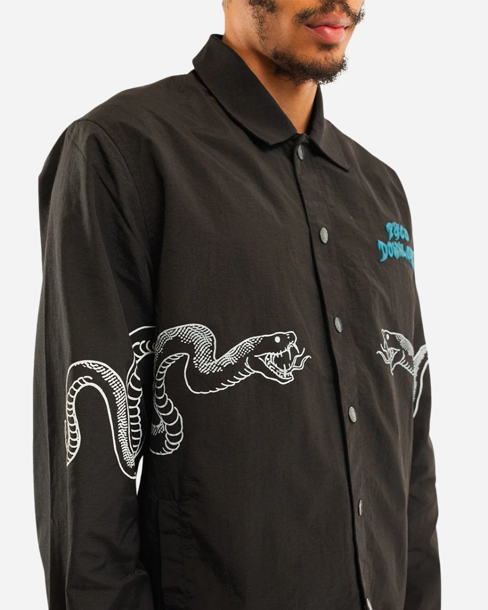 A man wears the P&Co Coach Jacket by 2025—a black button-up with a white snake graphic wrapping around the sleeve and side, plus blue text on the chest. His face is partially out of frame.