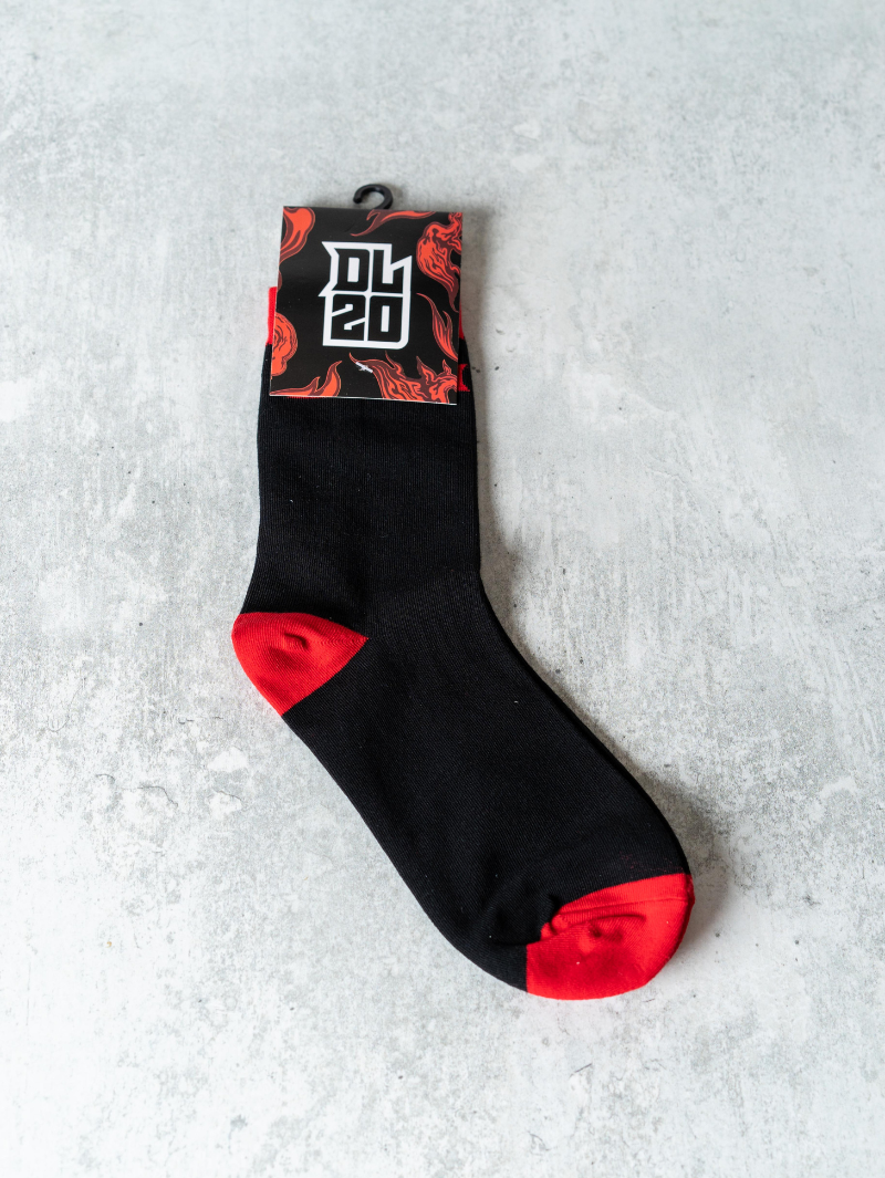 Black sock with red toe and heel detailing, displayed against a grey surface with branded packaging labelled "DL20" in bold white text over a flame-themed background.