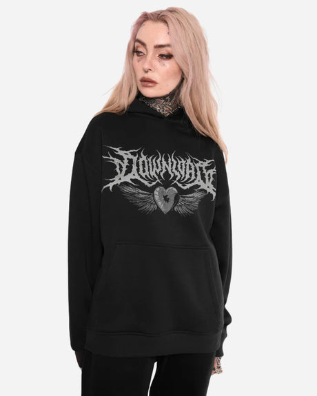 A person with long, light pink hair wears the Mary Wyatt Next Gen Pullover Hoodie by 2025, featuring a gothic DOWNWARD logo, wings, and heart graphic. They stand against a plain white background, looking to the side.