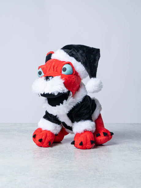 Festive red plush Download Dog dressed in a black and white Santa outfit with a matching Santa hat, featuring exaggerated cartoon-like features including bright blue eyes, sharp white teeth, and black clawed paws.