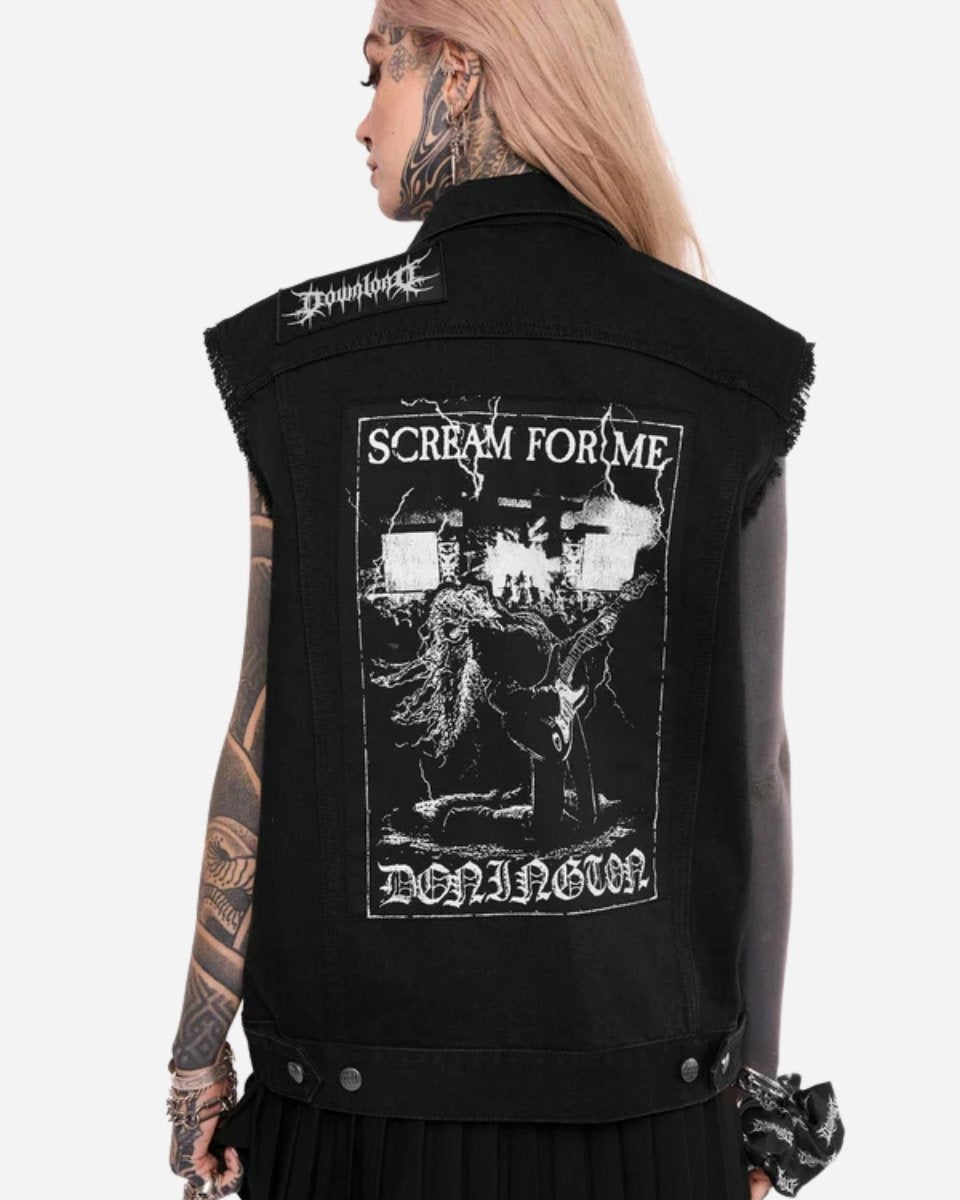 A person with tattoos and pink hair wears the Mary Wyatt Patch Lord Battle Jacket by 2025, a sleeveless black denim vest featuring a large patch on the back reading SCREAM FOR ME and DOWNHORN, with graphics of figures and buildings.