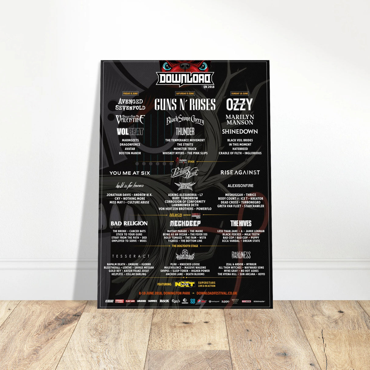The Download 2018 Line Up Poster A2 from Download Festival Shop features headliners Avenged Sevenfold, Guns N’ Roses, and Ozzy Osbourne, plus other bands in white text on black, propped against a white wall.
