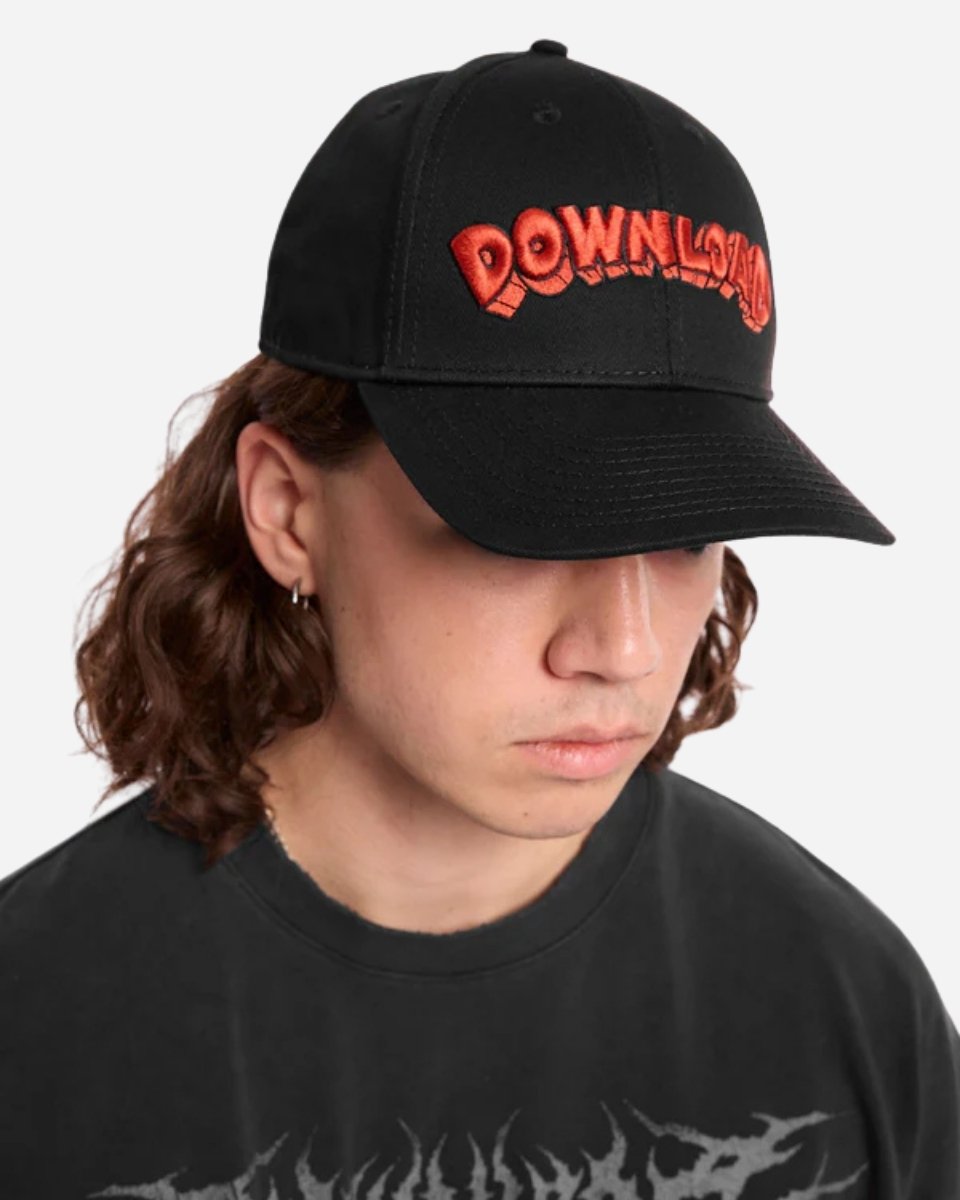 Young person with long brown hair wears the Mary Wyatt Welcome to Paradise Cap by 2025, a black cap with bold red lettering, plus a black graphic tee and small hoop earring, looking down against a plain background.