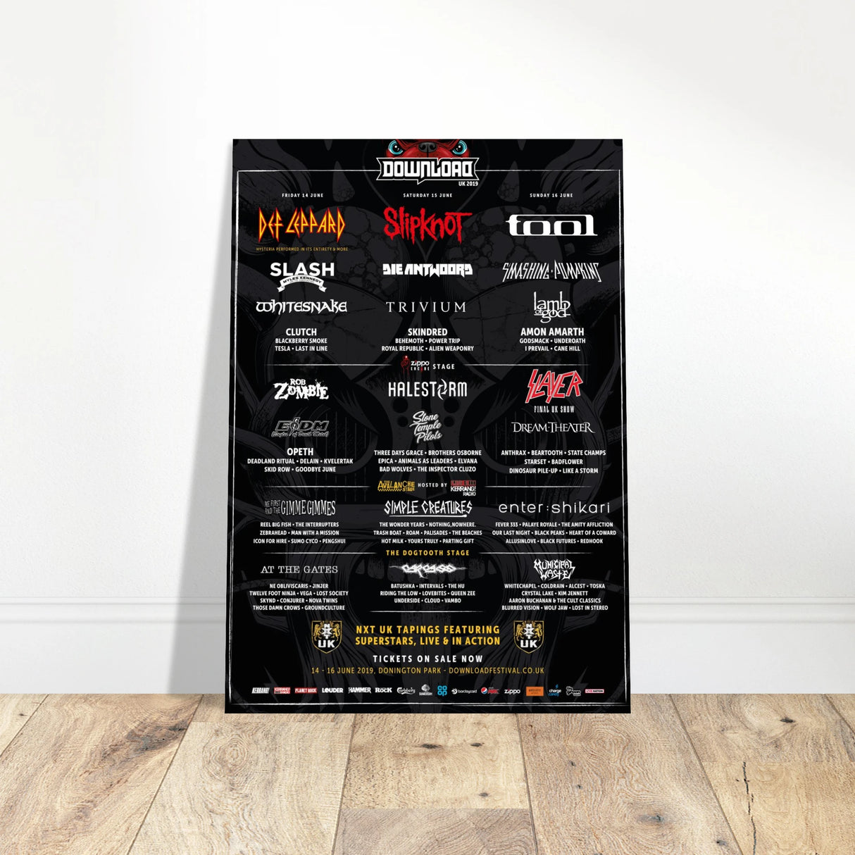 The Download Festival Shops Download 2019 Line Up Poster A2, featuring bands like Def Leppard, Slipknot, Tool, Slash, and Slayer, is framed and displayed against a white wall on a wooden floor.