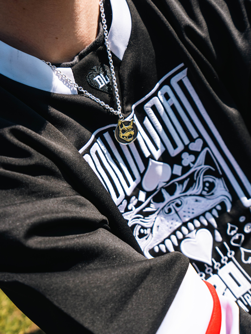 Close-up of a person wearing the Download x ParabellumLDN sterling silver pendant necklace, featuring a snarling dog head design on a circular charm, paired with a black and white Download festival jersey displaying a bold graphic of a dog face and playing card suits.
