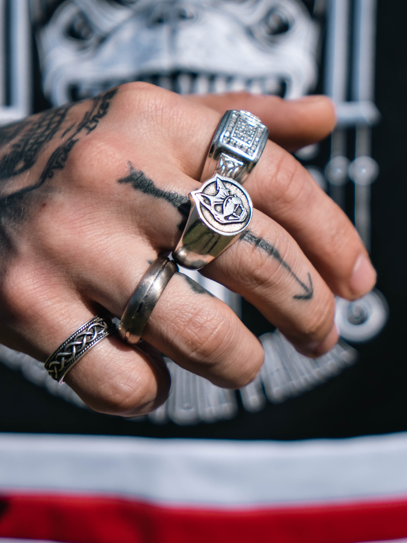 Close-up of a tattooed hand wearing multiple rings, with the central focus on the Download x ParabellumLDN sterling silver ring featuring an engraved snarling dog head.