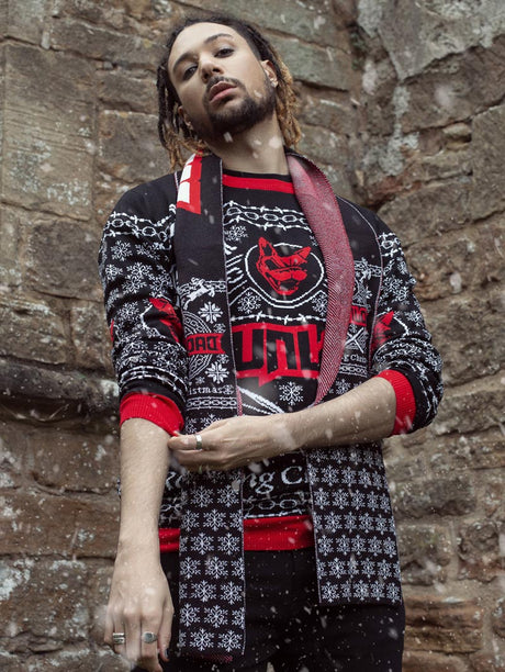 A person wearing a black festive jumper with red and white detailing, featuring the Download Festival logo, a snarling dog head, snowflakes, skeleton reindeer, and the words "Rocking Christmas." They are also wearing a matching festive scarf with snowflake patterns. Snow is falling gently in the scene.
