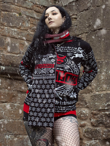 A person standing in front of a stone wall in falling snow, wearing a black festive sweater and matching scarf with red and white "Download" branding and snowflake patterns. The scarf says "Rocking Christmas".