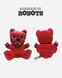 Two views of the Hand Made by Robots Download Vinyl Dog from Download 2026—a red, dog-like figure with black accents in a knit-style design, arms raised. The front shows a wide smile; the back has a tag. Text: HANDMADE BY ROBOTS.