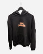 The P&Co Unisex Cerberus Hoodie by 2025 is a black hooded sweatshirt with a large front pocket, displayed on a hanger. It features a stylized orange and white graphic logo centered on the chest.