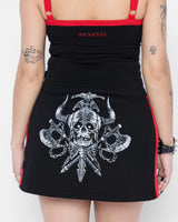 A tattooed person, seen from the back, wears a black Mary Wyatt Defender Sweatskirt by Download 2026 with red accents, a large horned skull graphic with crossed swords and axes, a matching tank top, and a studded bracelet.