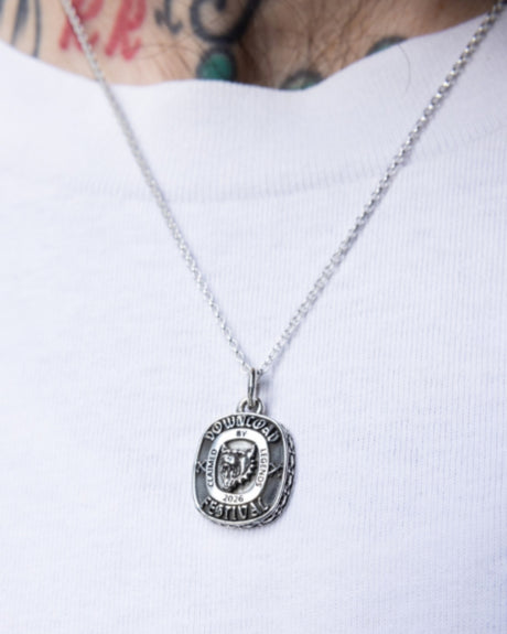 A close-up of a person wearing the TGF x Download Necklace by Download 2026 over a white shirt, with tattooed skin visible above the collar.
