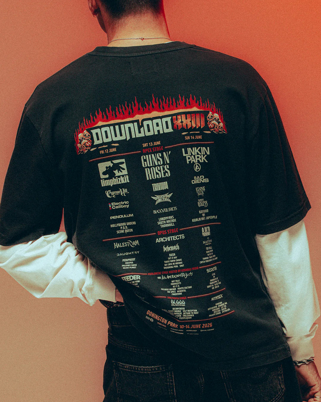 Someone faces away from the camera wearing a black P&Co Line Up T Shirt 2026 by 2026, featuring the festival lineup—including Limp Bizkit, Guns N’ Roses, and Linkin Park—on a red gradient background.
