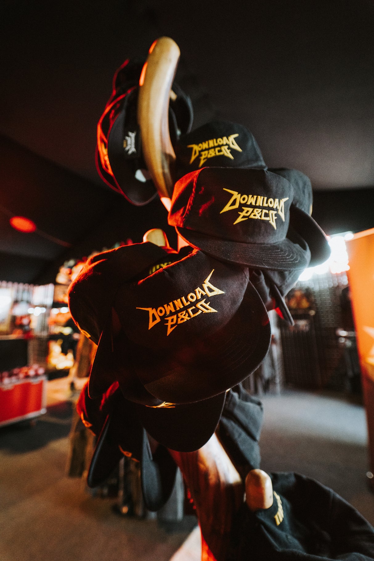 Several P&Co Logo Caps by Download 2026, featuring yellow logos on black fabric, are displayed on a wooden rack inside a warmly lit store.