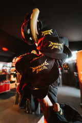 Several P&Co Logo Caps by Download 2026, featuring yellow logos on black fabric, are displayed on a wooden rack inside a warmly lit store.