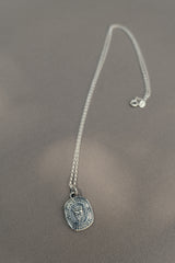 The TGF x Download Necklace by Download 2026 features a silver round pendant engraved with an owl and the phrase "Knowledge is Power," displayed on a soft, neutral surface.
