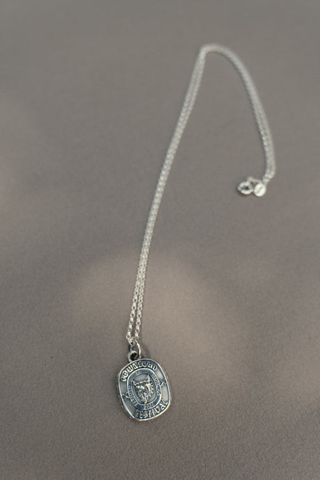 The TGF x Download Necklace by Download 2026 features a silver round pendant engraved with an owl and the phrase "Knowledge is Power," displayed on a soft, neutral surface.