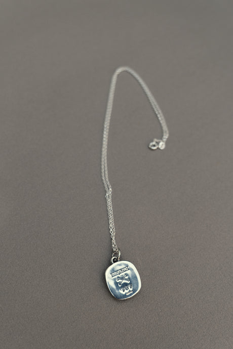 The TGF x Download Necklace by Download 2026 features a thin silver chain and a square pendant engraved with an octopus and the word "HYPNOSIS," shown resting on a gray surface.