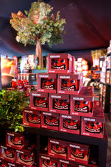 A display of stacked red Dog Head Shaped Mugs by Download 2026, featuring cartoon monster faces, set on black shelves in a shop with artificial plants and trees in the background.